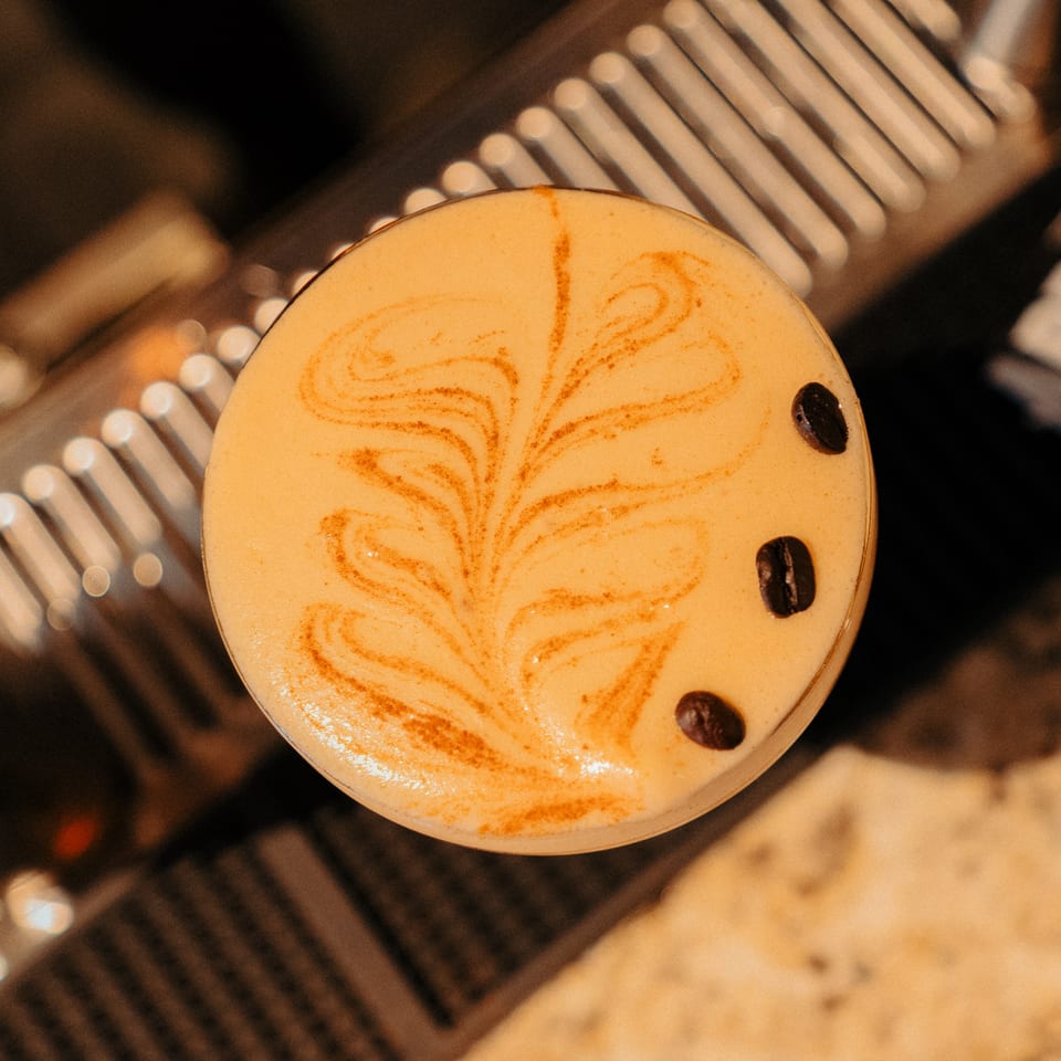 Close-up of a Cafe COPA espresso martini with latte art and three coffee beans.