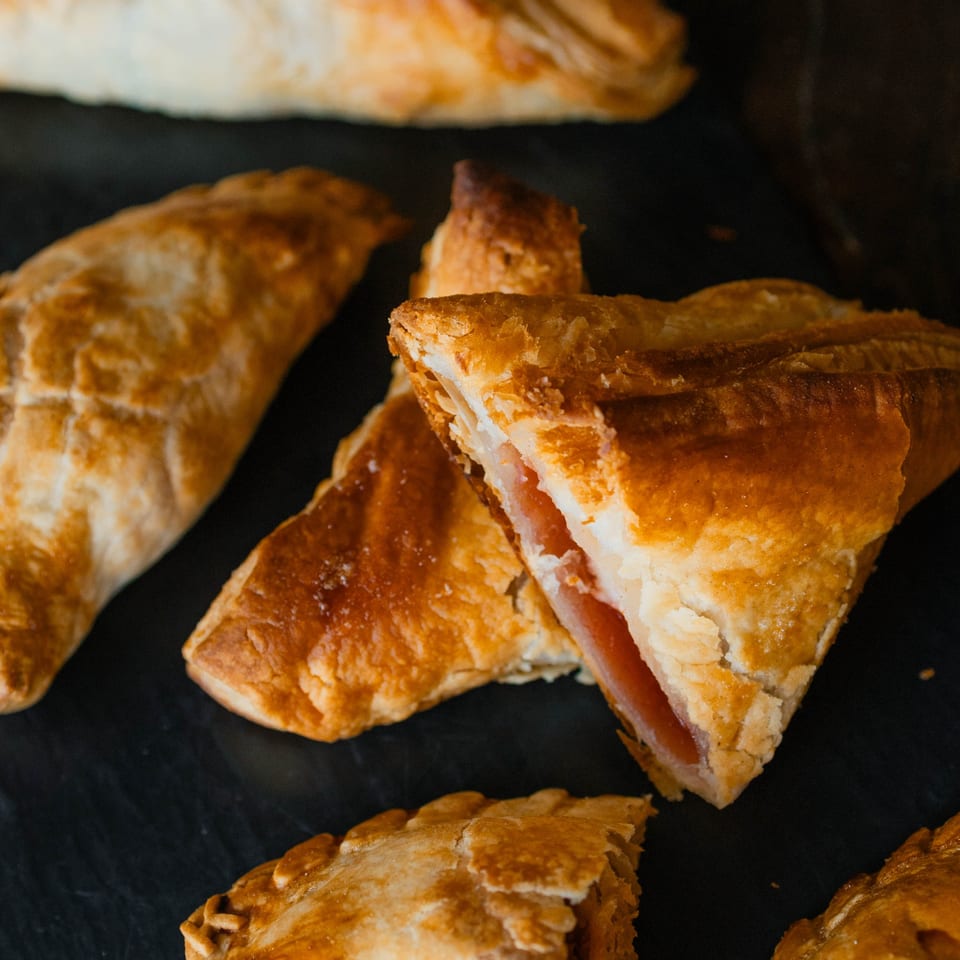 Golden-brown pastries, one sliced open revealing ham and cheese filling, on a dark surface.