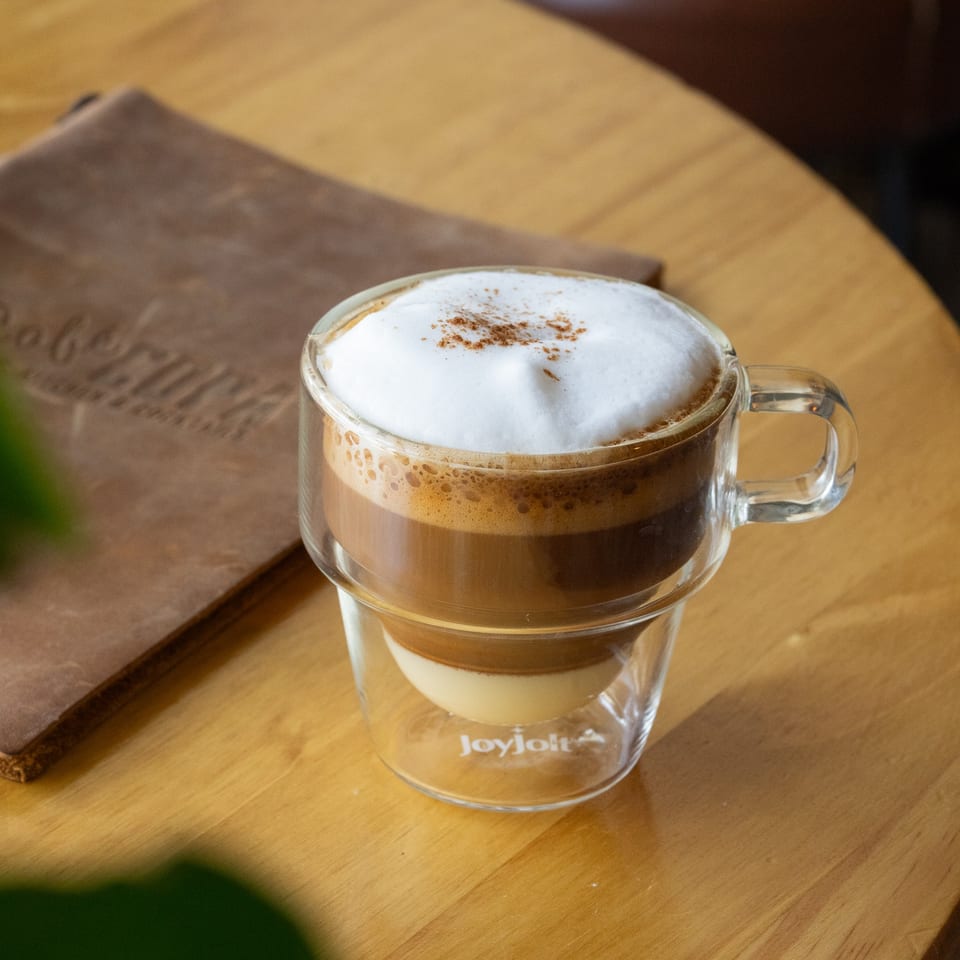 A Cafe COPA latte with frothy milk and cinnamon on a wooden table next to a menu.