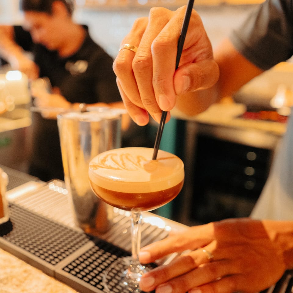 A barista stirs a coffee cocktail with latte art at Cafe COPA.