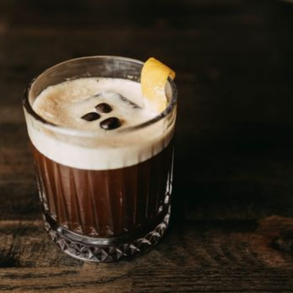 Cafe COPA's espresso martini with foam, coffee beans, and a lemon twist on a wooden table.