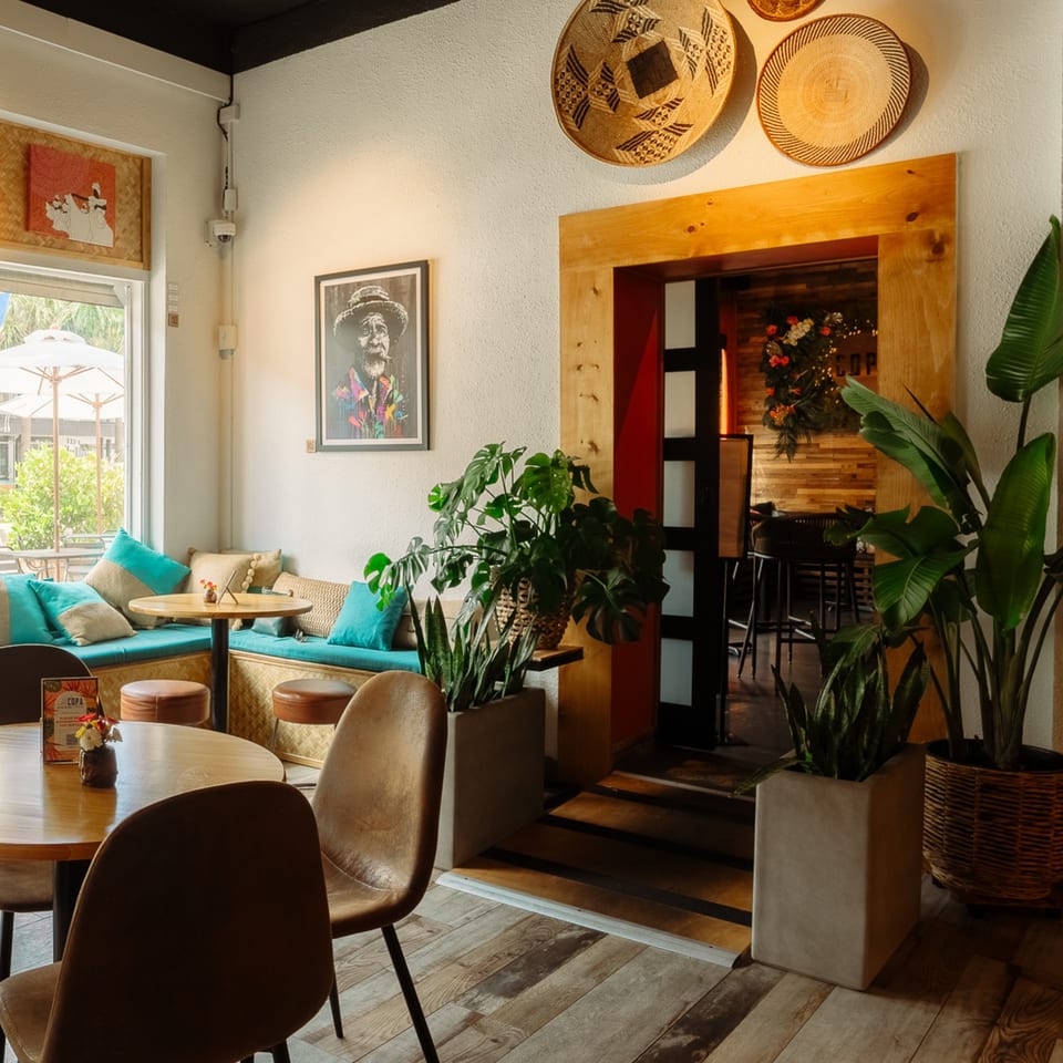 Cafe COPA's interior features a cozy seating area with turquoise cushions, wooden tables, and potted plants.