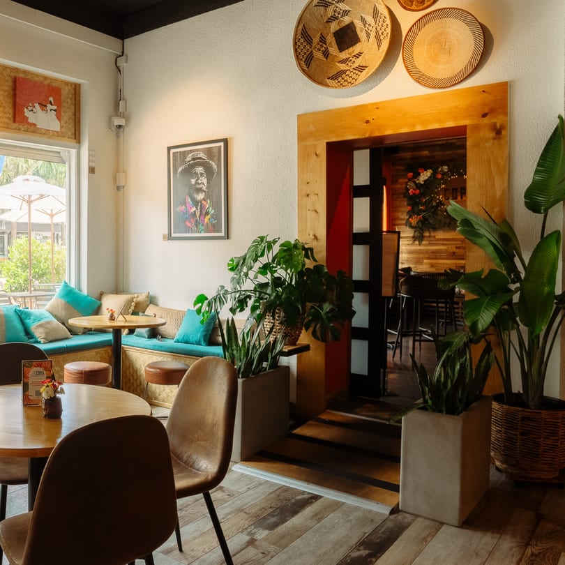 Cafe COPA's interior features a cozy seating area with turquoise cushions, wooden tables, and potted plants.