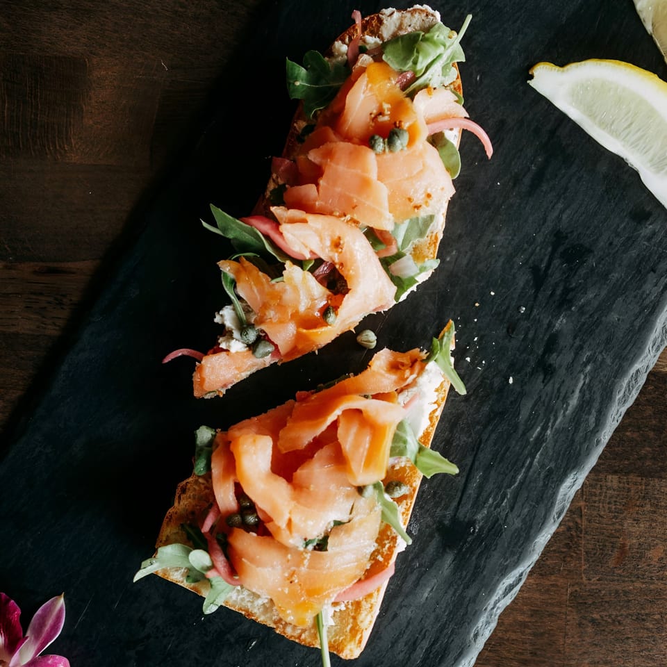 Two pieces of Cafe COPA's smoked salmon bruschetta with capers, arugula, and red onion.
