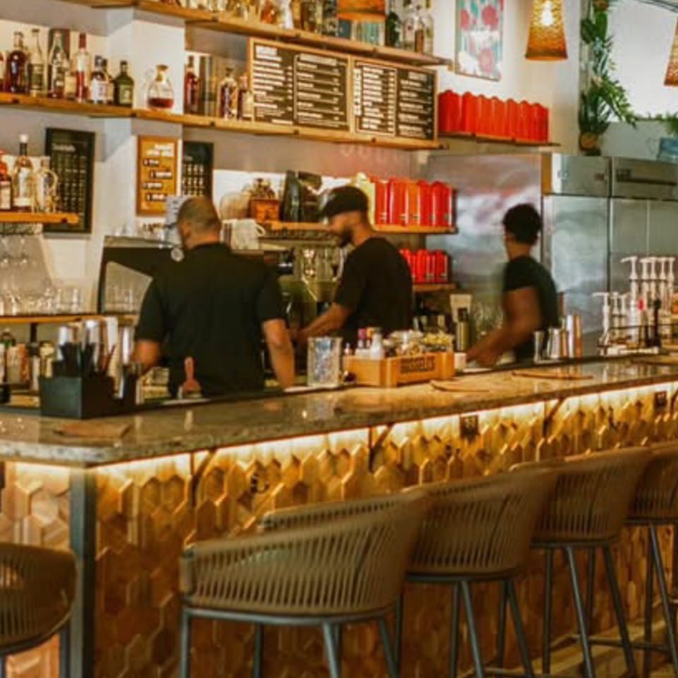 Cafe COPA bar with three baristas working, shelves of bottles, and hexagon-patterned bar front.