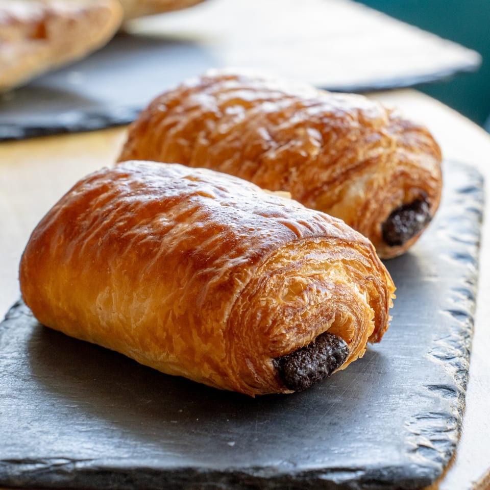 Two golden-brown chocolate croissants on a dark slate serving board.