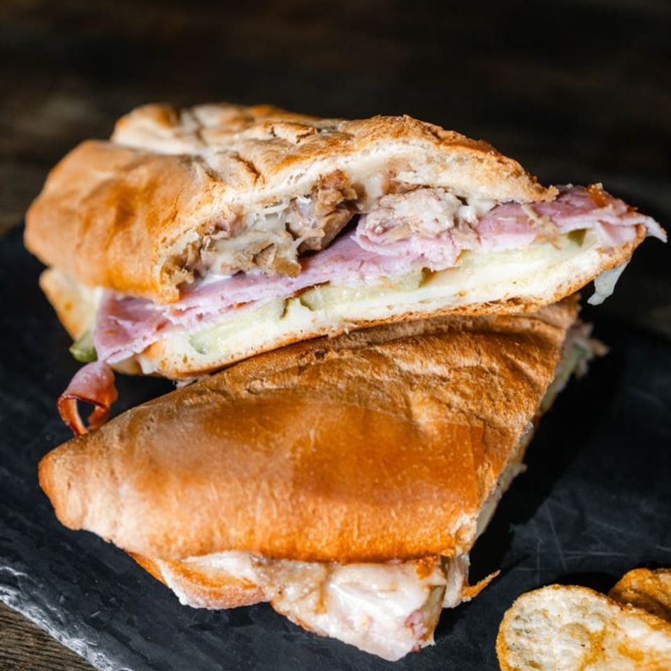 A sliced Cuban sandwich with ham, cheese, and pork on toasted bread, served on a dark slate.
